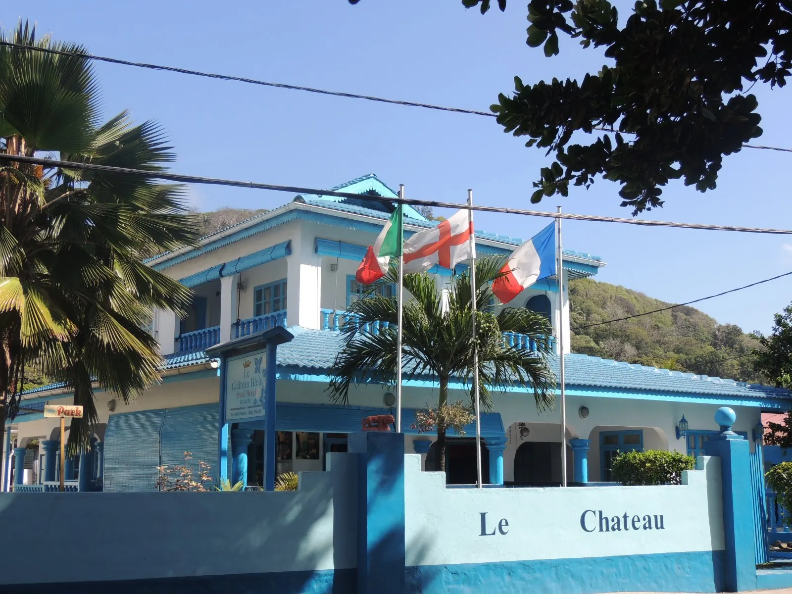 Le Chateau Bleu, ein zweistöckiges blau-weiß gestrichenes Haus mit Flaggen entlang der Vordermauer